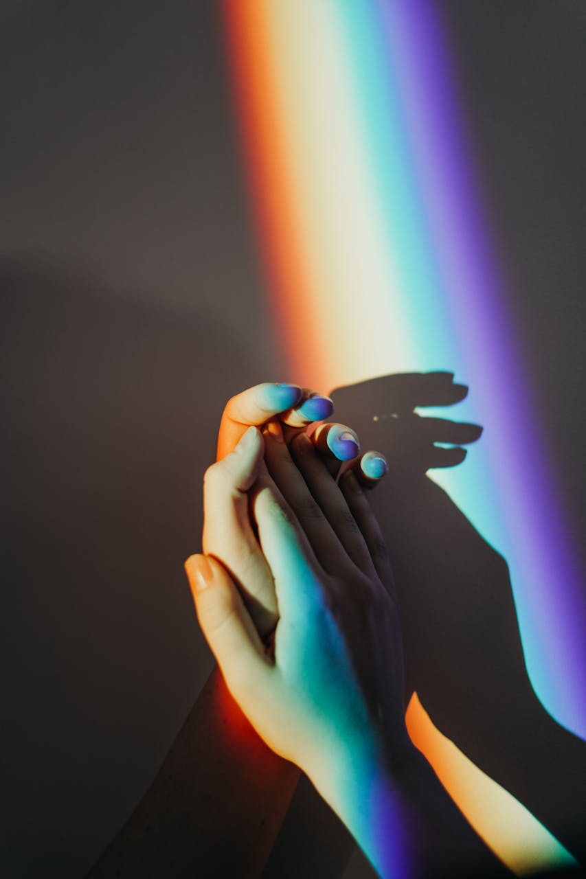 hands clapping against a rainbow prism effect of light